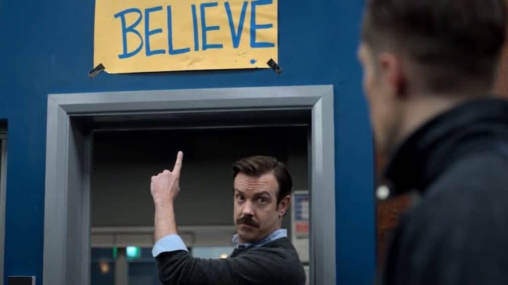 Ted Lasso pointing at beleive sign